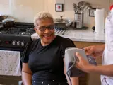 A woman in her own home smiling and laughing with a nurse holding a blood pressure monitor